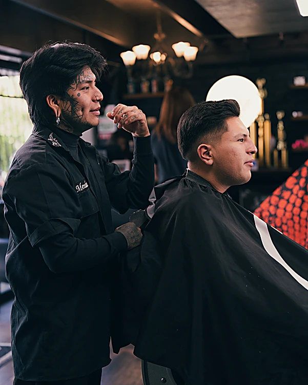 Barbero con camisa negra revisando el corte de un cliente de perfil, bajo la luz cálida de un candil