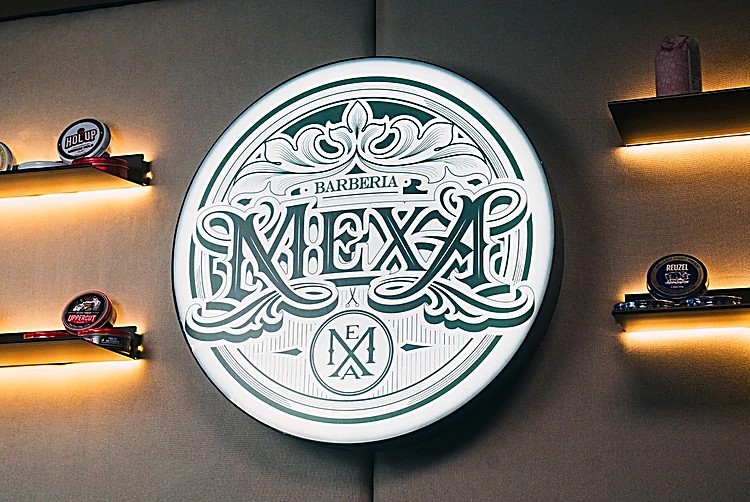 Sucursal Condesa: el letrero redondo de MEXA en verde sobre el muro gris, entre repisas con luz y latas de pomada