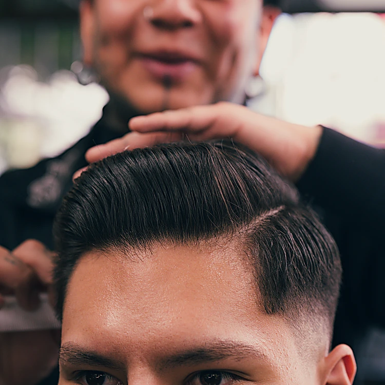 Cierre de un degradado bajo con raya marcada al lado; las manos del barbero acomodan el peinado